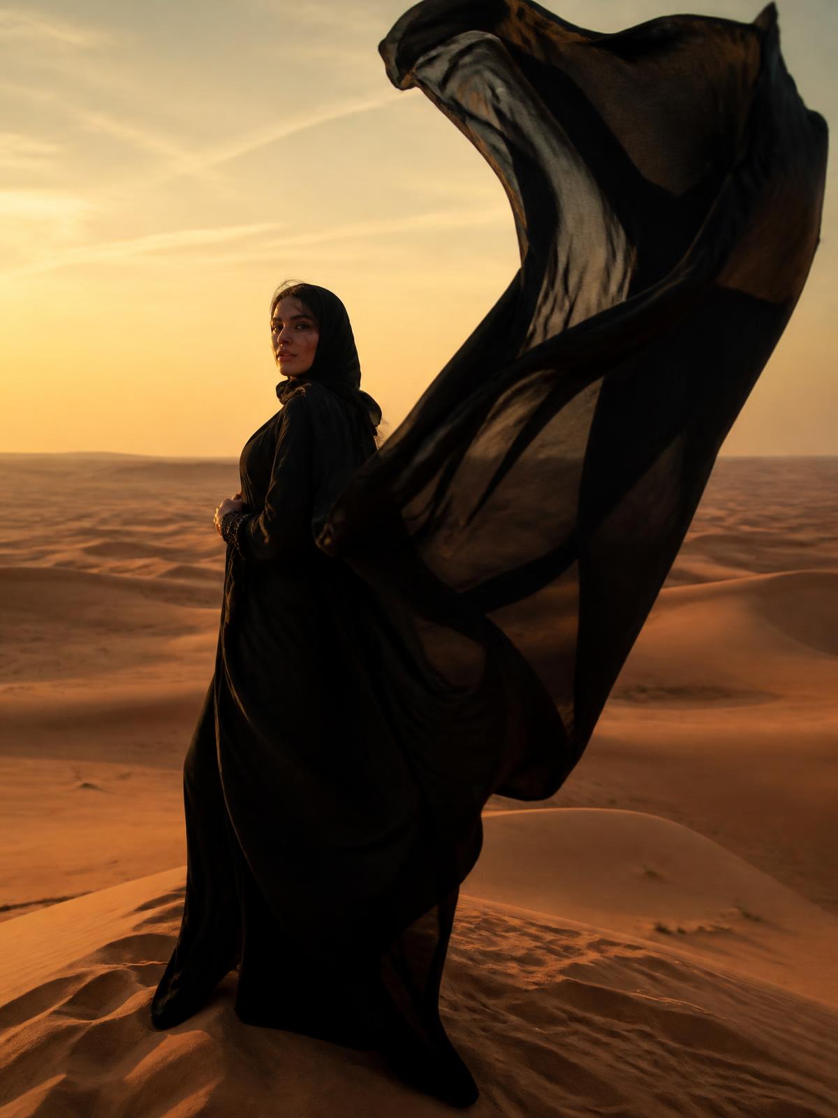 A woman in a billowing black silk abaya gown on a desert dune
